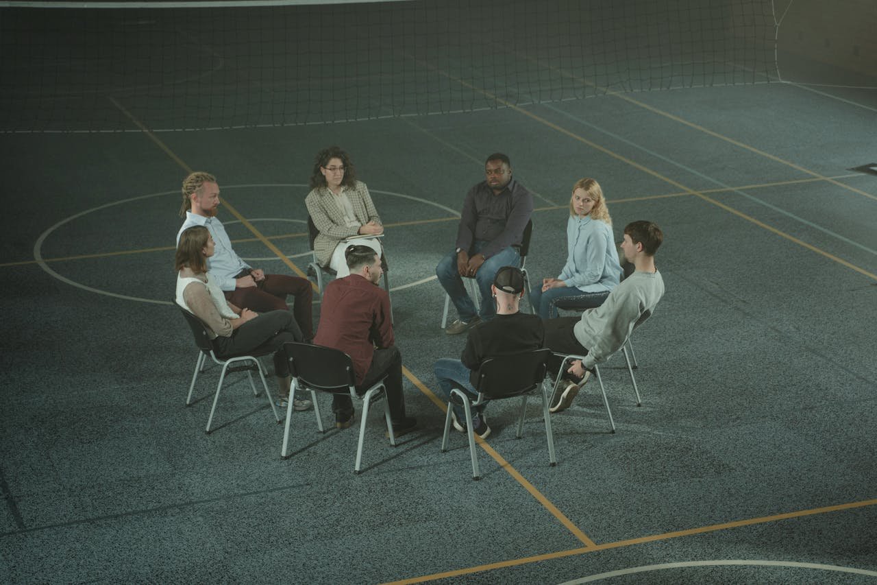 A diverse group of people sitting in a circle during a therapy session in a sports hall.