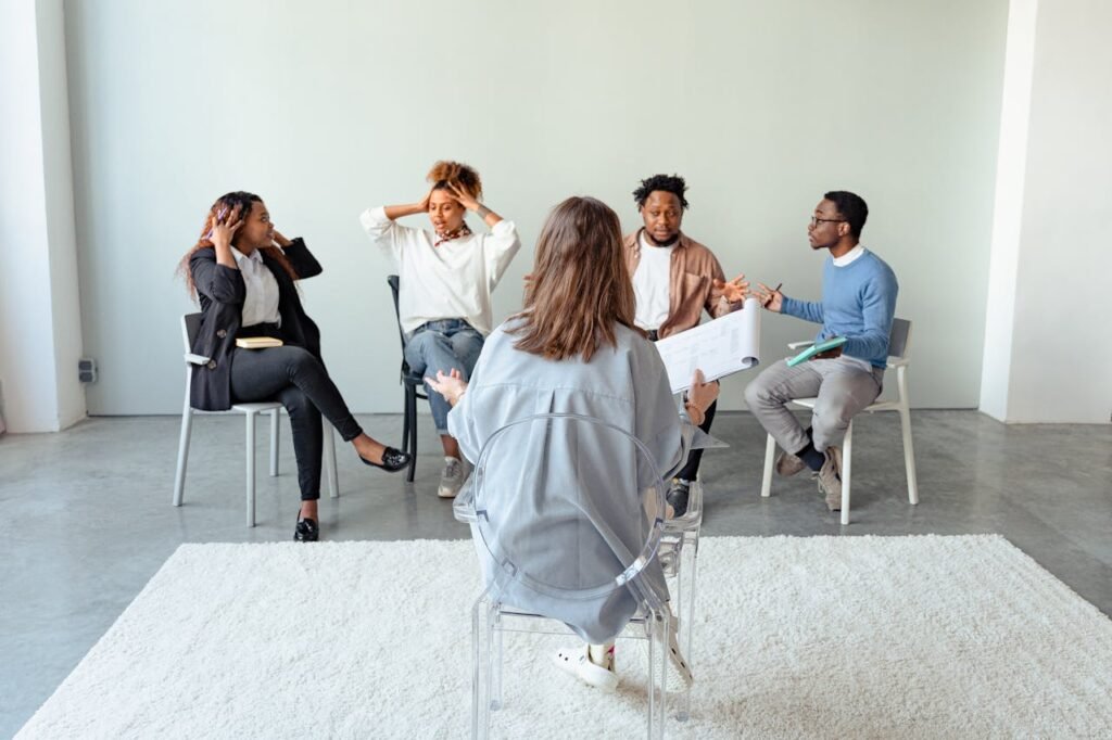 People engaging in a group therapy session indoors, discussing mental health topics.